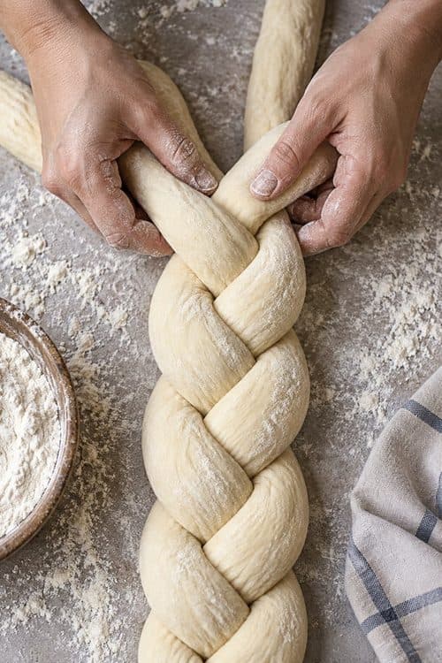 Hands braiding a loaf of dough on a floured table